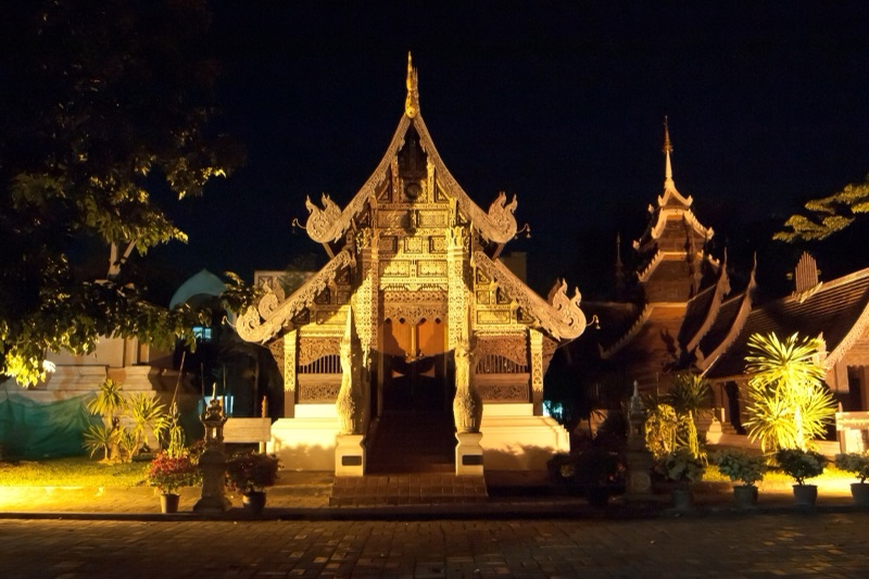 วิหารไม้แกะสลักปิดทองแบบล้านนาในวัดเจดีย์หลวง เชียงใหม่ ยามค่ำคืน แสงไฟส่องหน้าบันและนาคคู่ที่บันได ไม่มีผู้คน