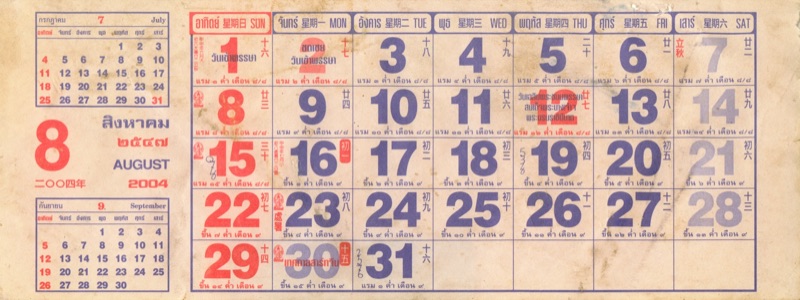A Thai wall-calendar page for August 2004 with large date numbers and the waxing or waning lunar day printed under every date