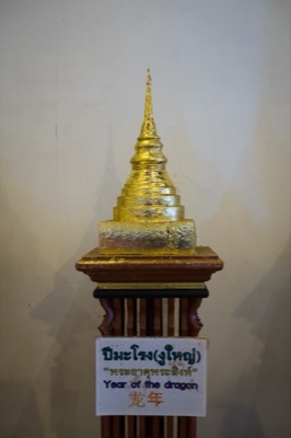 Gilded model chedi on a wooden stand, its sign naming the naga (dragon) year relic, at Wat Phra Singh, Chiang Mai