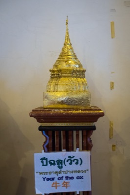 Gilded model chedi on a wooden stand, its sign naming the ox year relic, at Wat Phra Singh, Chiang Mai
