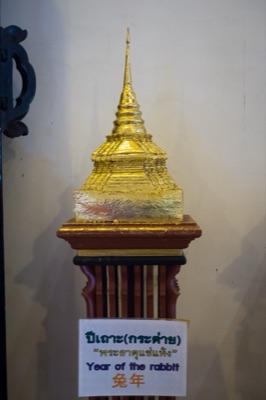 Gilded model chedi on a wooden stand, its sign naming the rabbit year relic, at Wat Phra Singh, Chiang Mai