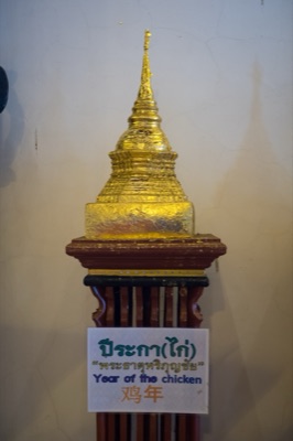 Gilded model chedi on a wooden stand, its sign naming the rooster year relic, at Wat Phra Singh, Chiang Mai