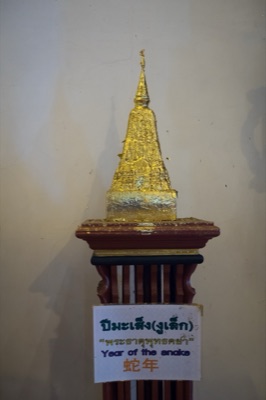 Gilded model chedi on a wooden stand, its sign naming the snake year relic, at Wat Phra Singh, Chiang Mai