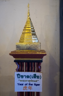 Gilded model chedi on a wooden stand, its sign naming the tiger year relic, at Wat Phra Singh, Chiang Mai