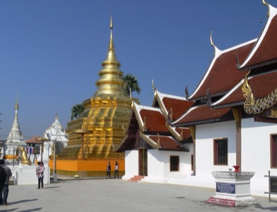 The golden chedi of Wat Phra That Si Chom Thong beside a red-roofed hall