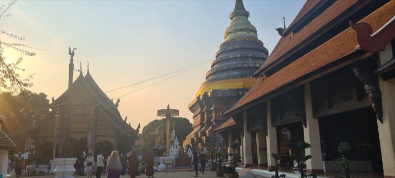ลานวัดพระธาตุลำปางหลวงยามเย็น เจดีย์ทรงล้านนาสีทองตั้งเด่นกลางลาน มีวิหารไม้หลังคาซ้อนชั้นอยู่สองข้าง