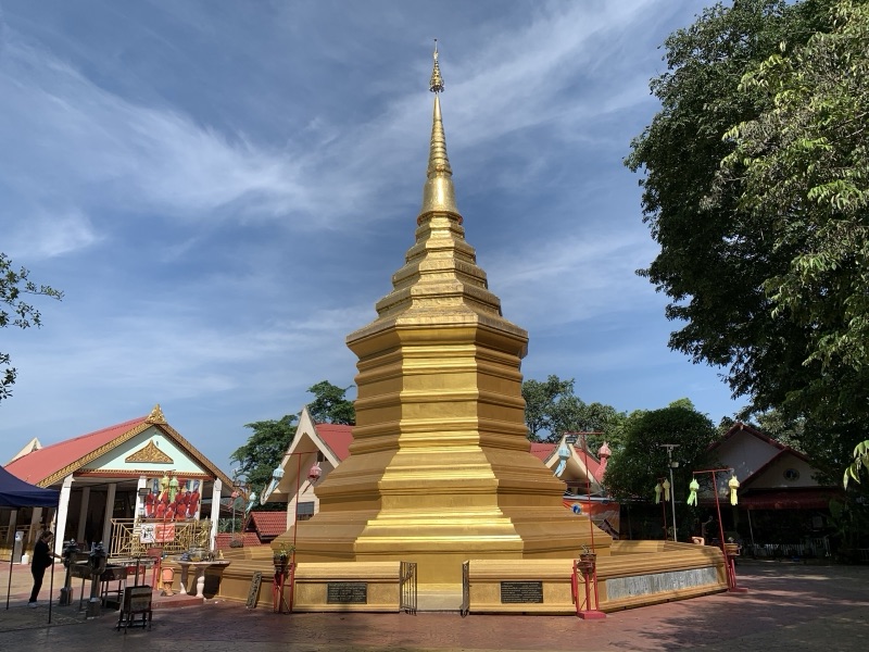 The golden Lanna-style chedi of Phra That Doi Chom Thong on a temple courtyard under a blue sky, surrounded by pavilions and trees