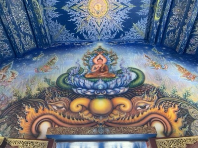 Blue-toned murals on the ceiling and walls of the vihara at Wat Rong Suea Ten, with a Buddha seated on a lotus in the centre