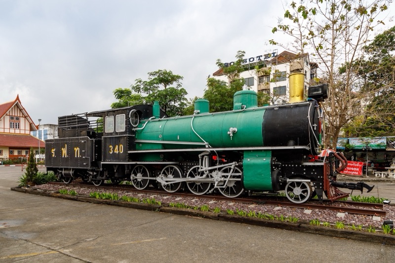 A green and black steam locomotive on display on a short track at Chiang Mai railway station