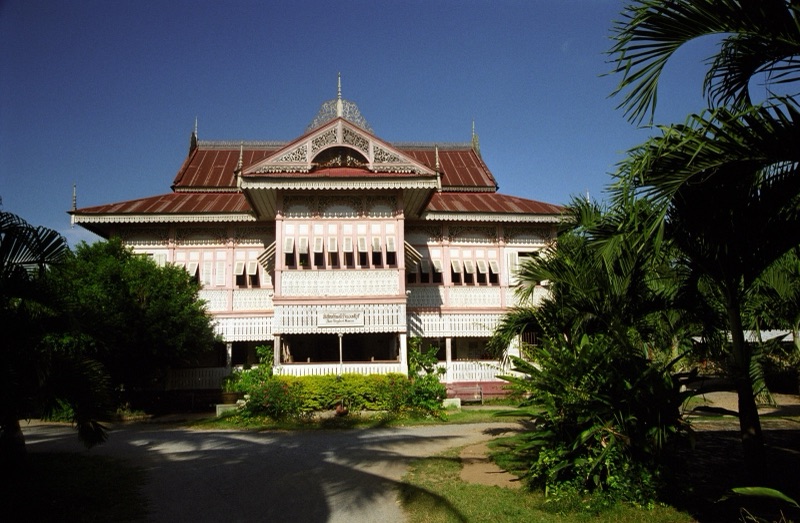 Vongburi House in Phrae, a two-storey teak house painted pale pink, its gables and eaves decorated with white gingerbread fretwork, with a lawn and trees in front