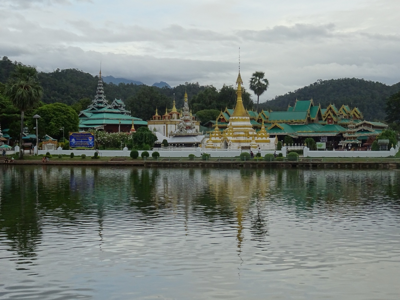 Wat Chong Klang and Wat Chong Kham on the edge of a lake, golden stupas and tiered Tai Yai roofs reflected in the water, with mountains behind