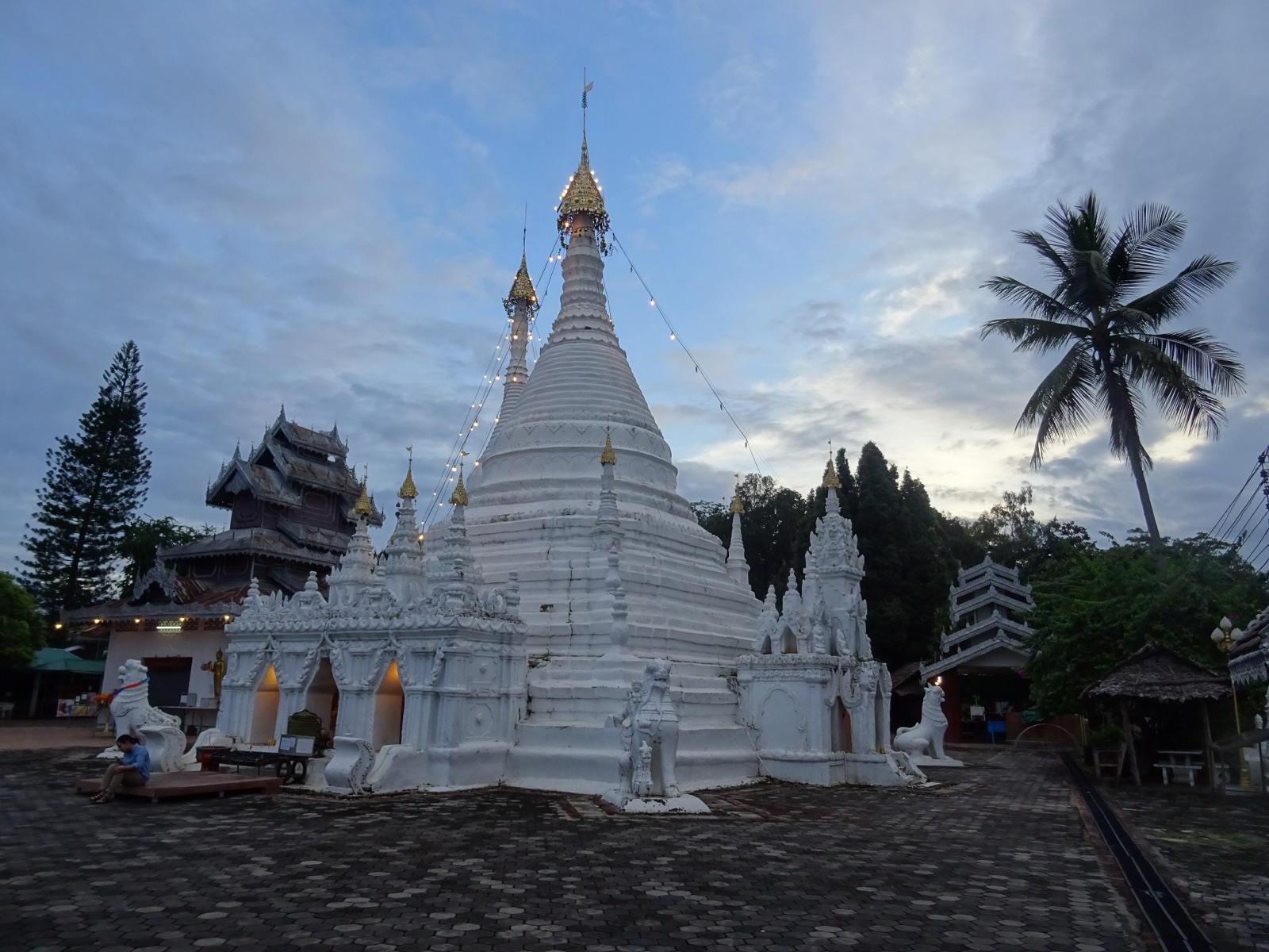 A white bell-shaped stupa with a golden spire on Doi Kong Mu, surrounded by small stupas and stucco lions, with a tiered Tai Yai roof behind