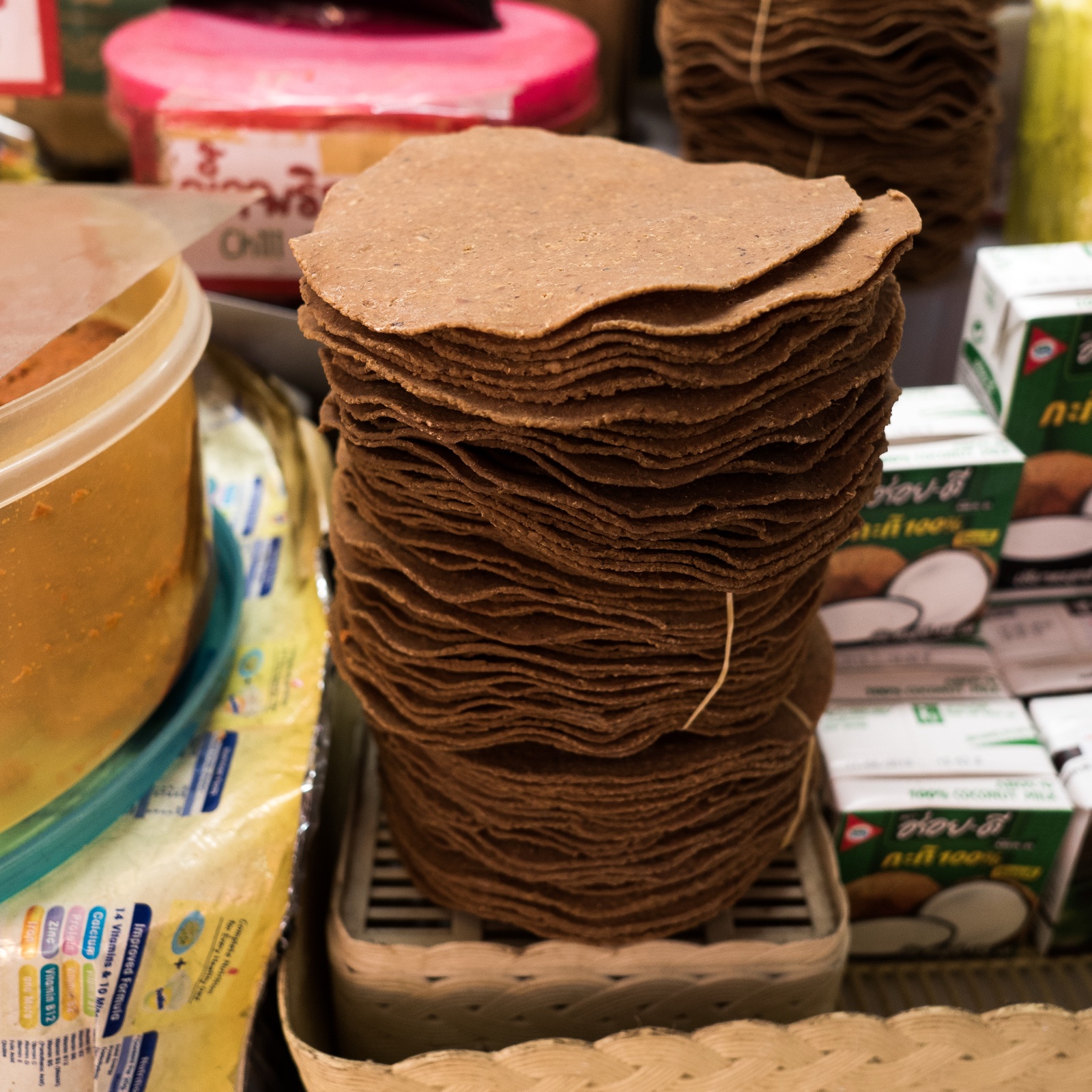 Reddish-brown discs of dried fermented soybean, round and flat, stacked high on a market stall