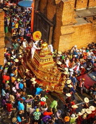 ขบวนแห่พระพุทธรูปบนบุษบกสีทองผ่านกำแพงเมืองเชียงใหม่ มีผู้คนรอสรงน้ำ มองจากที่สูง