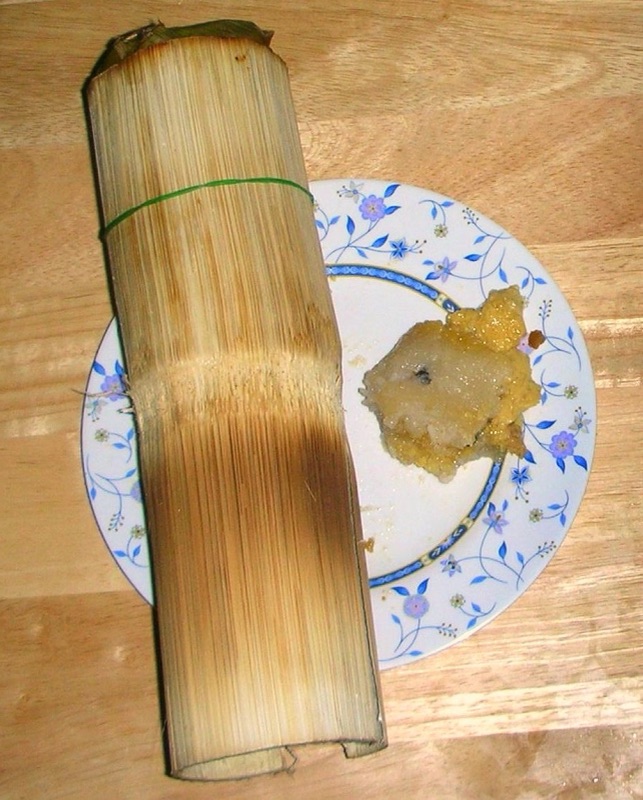 A tube of khao lam with the bamboo peeled down to a thin inner layer, lying on a flowered plate beside some khao lam already taken out
