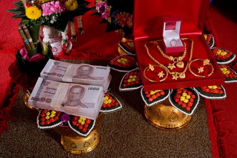 พานทองสองใบวางบนผ้าแดง ใส่ธนบัตรปึกหนึ่งและสร้อยทองพร้อมแหวน ตกแต่งด้วยดอกไม้