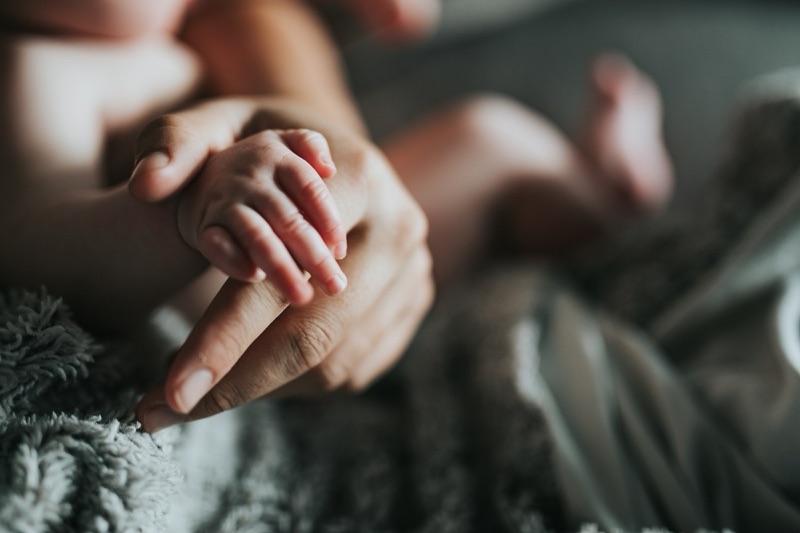 A newborn's tiny hand gripping an adult's finger on a soft grey blanket
