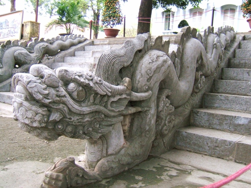 A stone balustrade carved as a long dragon, its open-mouthed head at the bottom and its scaly body curving up the steps