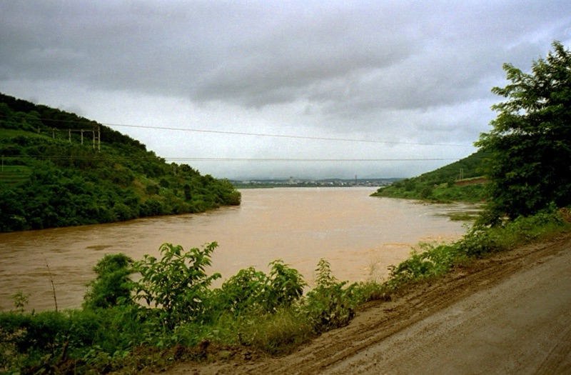 The brown Mekong flowing through green hills under a cloudy sky, with a town in the distance downstream
