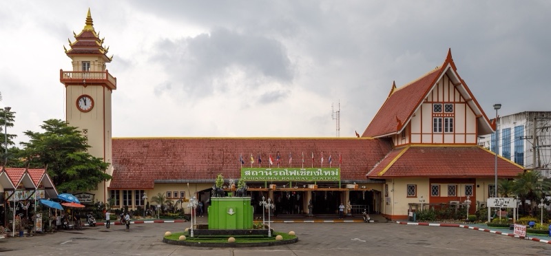 อาคารสถานีรถไฟเชียงใหม่ทรงยาว หลังคาสีแดง มีหอนาฬิกาสูงด้านซ้าย ลานหน้าสถานีกว้าง