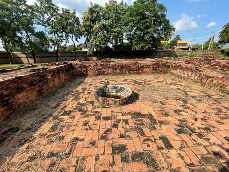 The red-brick foundations of an old church in the Portuguese village at Ayutthaya, with a brick floor and a round well in the middle, surrounded by tall trees under a blue sky