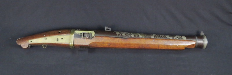 An old Japanese matchlock gun with a long iron barrel and a brown wooden stock, on a black background