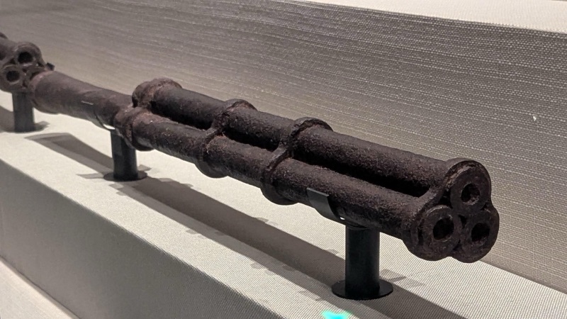 An old Ming-dynasty iron gun with three barrels bound together, on a stand in a museum display case