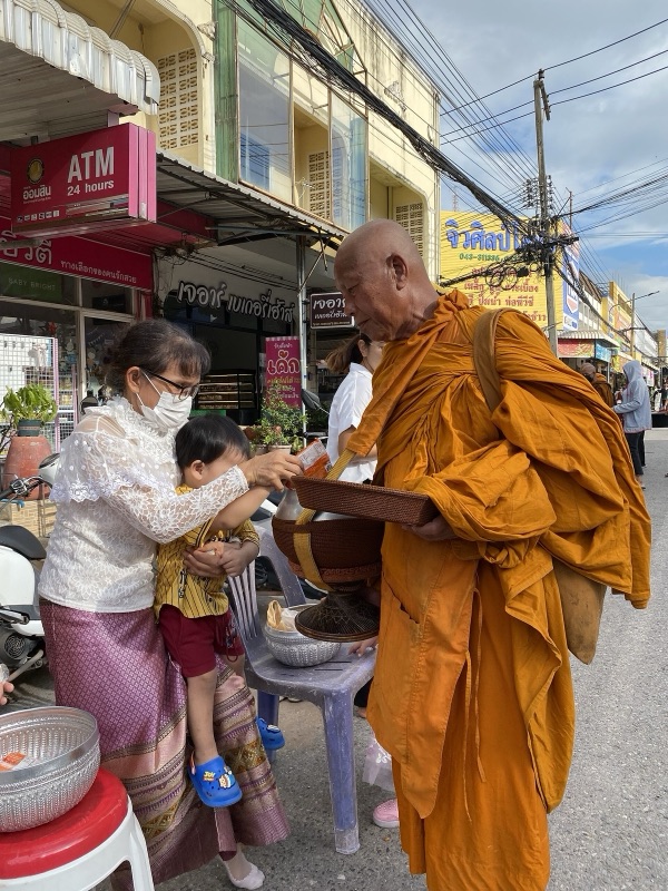 A grandmother holding her grandson as they give alms to a monk by the roadside in the morning