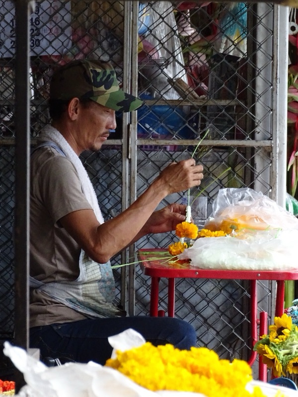 A man in a cap threading yellow marigolds into garlands at his stall in Warorot Market, Chiang Mai