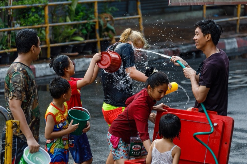 Children and adults laughing and splashing water on a street in Chiang Mai during Songkran