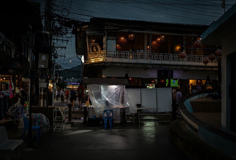 ซอยในเมืองเชียงใหม่ยามพลบค่ำ อาคารไม้สองชั้นเปิดไฟสว่าง ผู้คนเดินผ่านไปมาอยู่ไกล ๆ