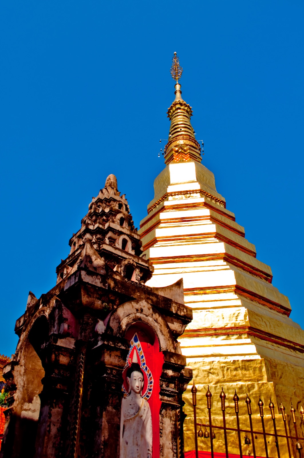 พระธาตุช่อแฮสีทองตั้งตระหง่านหลังซุ้มพระพุทธรูปเก่า จังหวัดแพร่