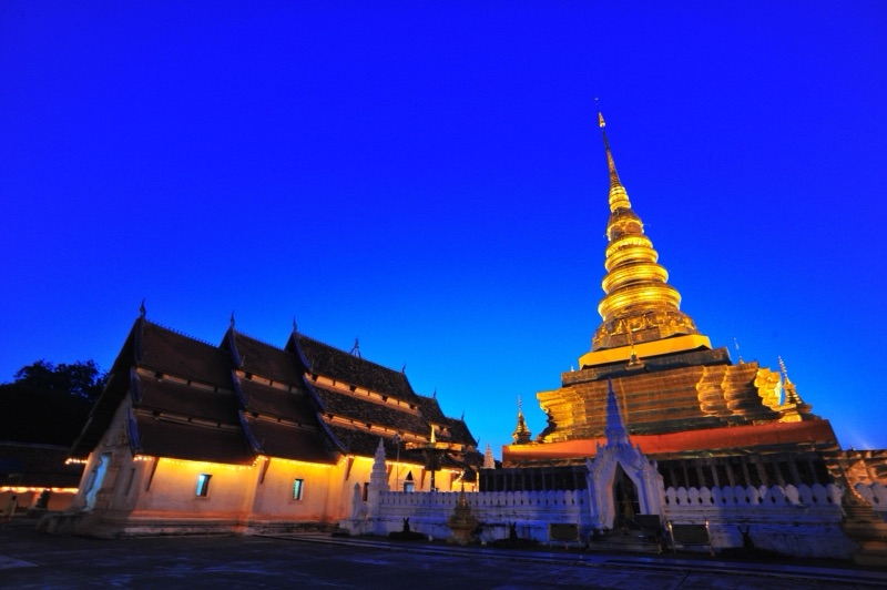 The golden Phra That Chae Haeng stupa behind a temple hall under a deep blue evening sky