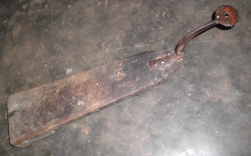 A long wooden bench-style coconut scraper with an iron blade at one end