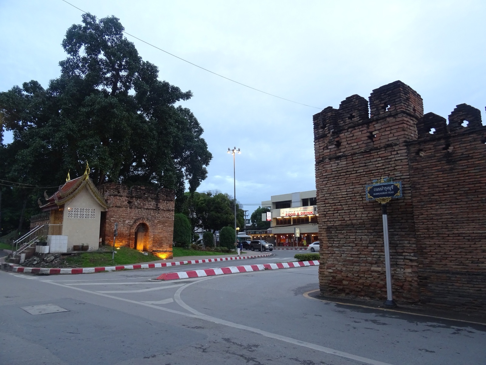 Chiang Mai Gate (Pratu Chiang Mai) at dusk, with the brick city wall and a small shrine beside a large tree