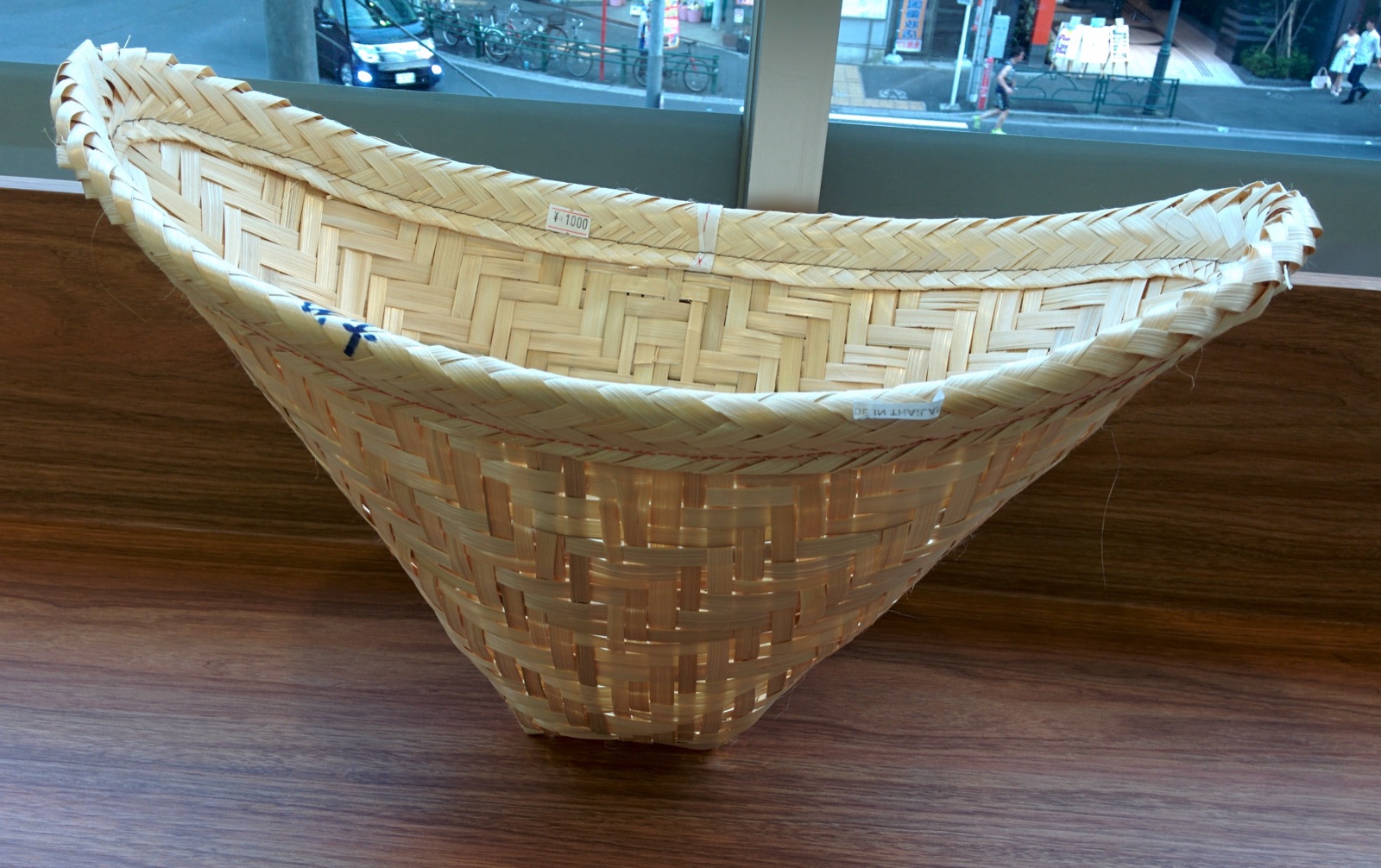 A cone-shaped woven bamboo steamer basket with a wide mouth on a wooden table