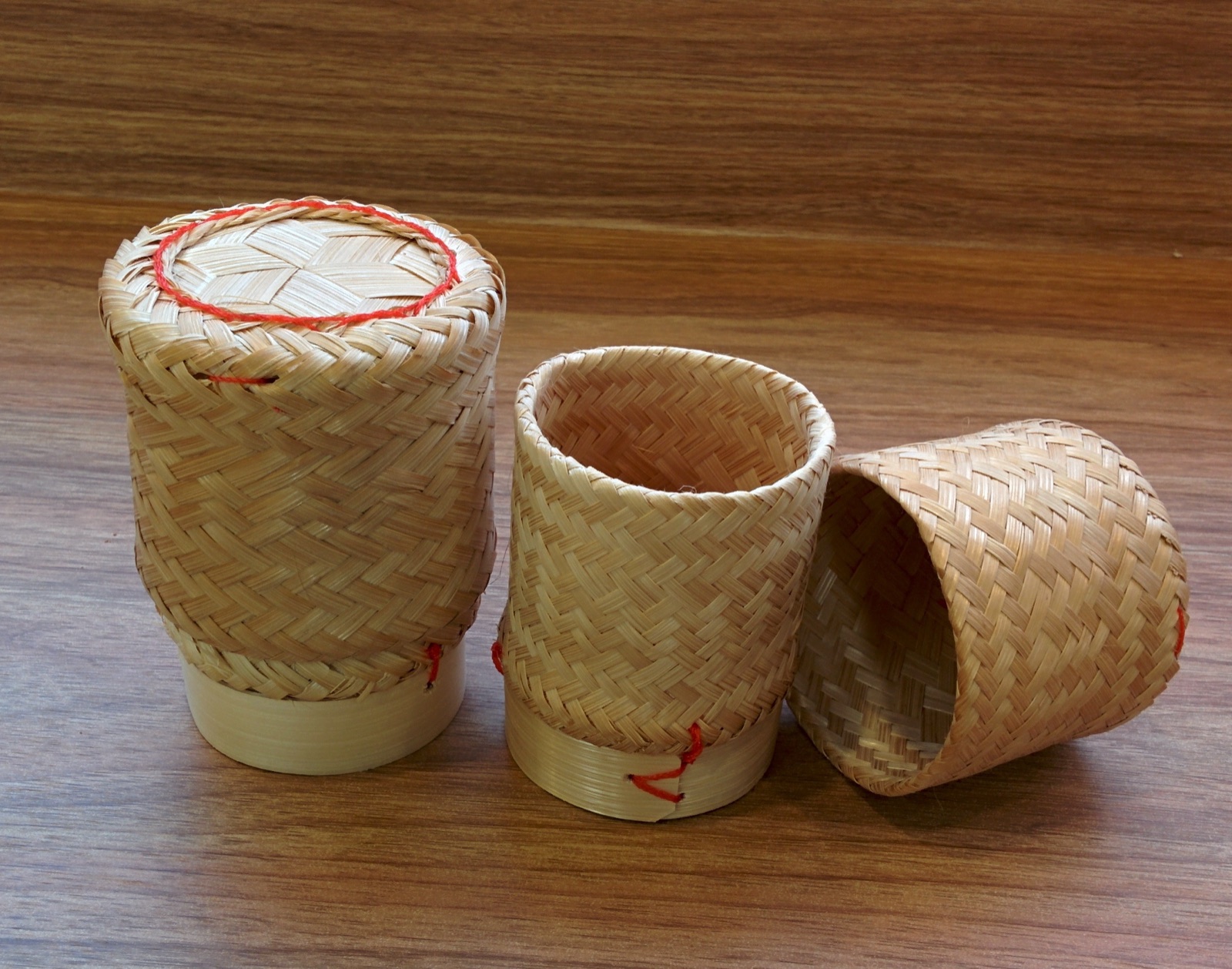 Three woven bamboo sticky-rice containers, one closed with a red-trimmed lid and two open