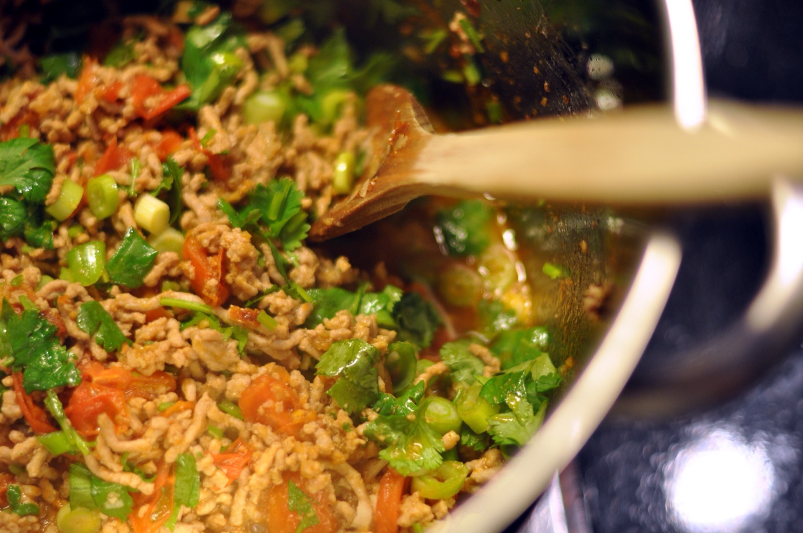 Nam phrik ong being stirred in a pot, with minced pork, tomato, coriander and sliced spring onion