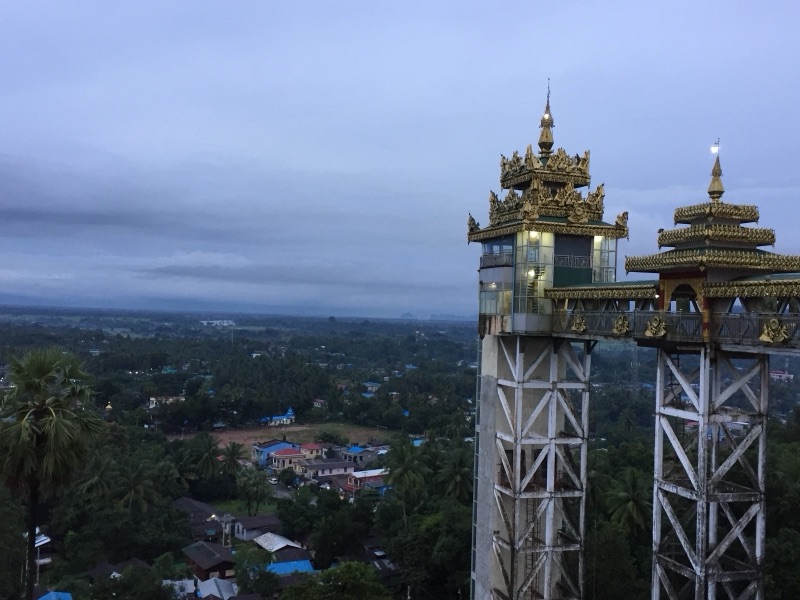 View from the hill of Kyaikthanlan Pagoda: two golden spired towers and the town of Mawlamyine among trees under a cloudy sky