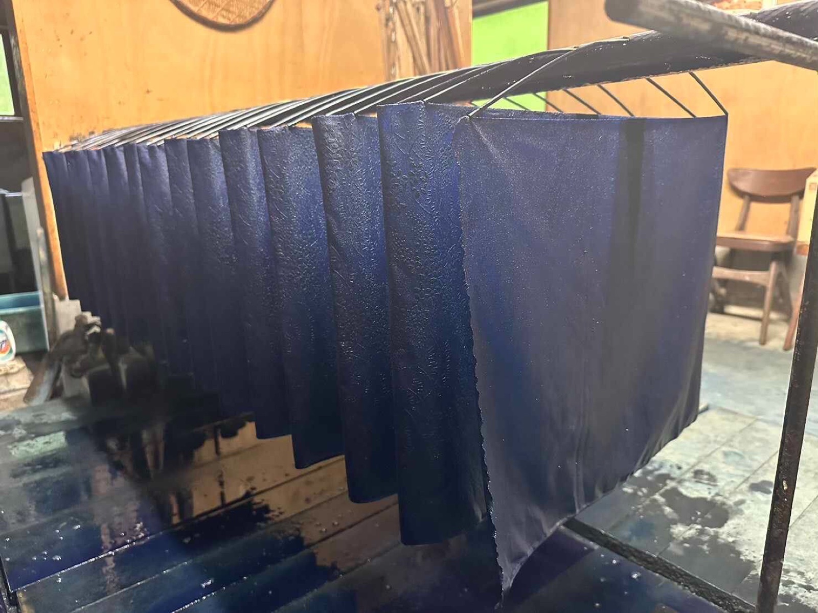 Freshly dyed dark-blue cloths hung in rows on a rack in a dye workshop, with blue stains on the wet floor