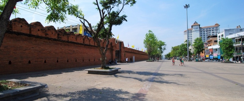 The red-brick wall of Chiang Mai's old city at Tha Phae Gate, with a large tree and a wide open square in front under a clear sky