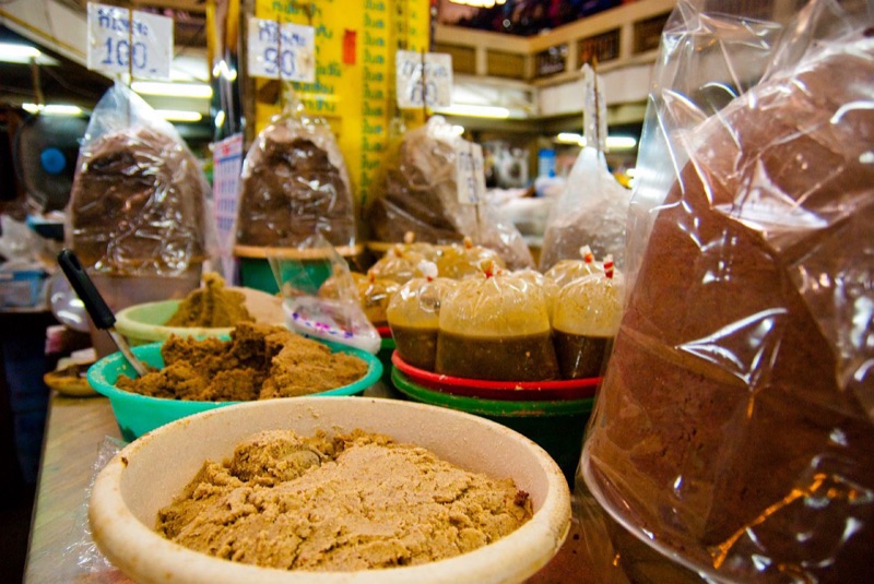 Shrimp paste and other fermented foods sold in bags and trays at Warorot Market (Kad Luang) in Chiang Mai, with price tags hanging above