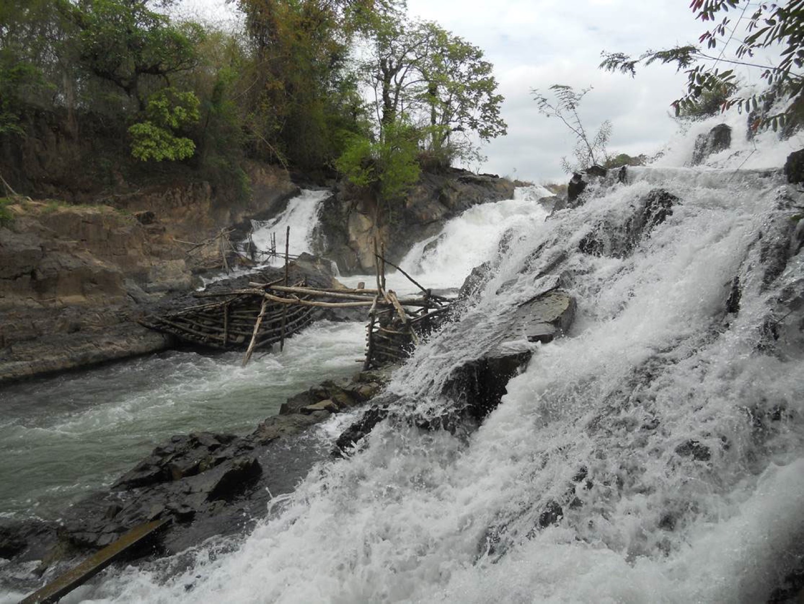 A timber fish-trap frame built across a channel beside a waterfall and rocky rapids on the Mekong near the Laos–Cambodia border