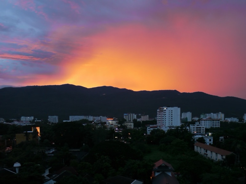 An orange and purple dusk sky over the Doi Suthep ridge, with the buildings and trees of Chiang Mai below