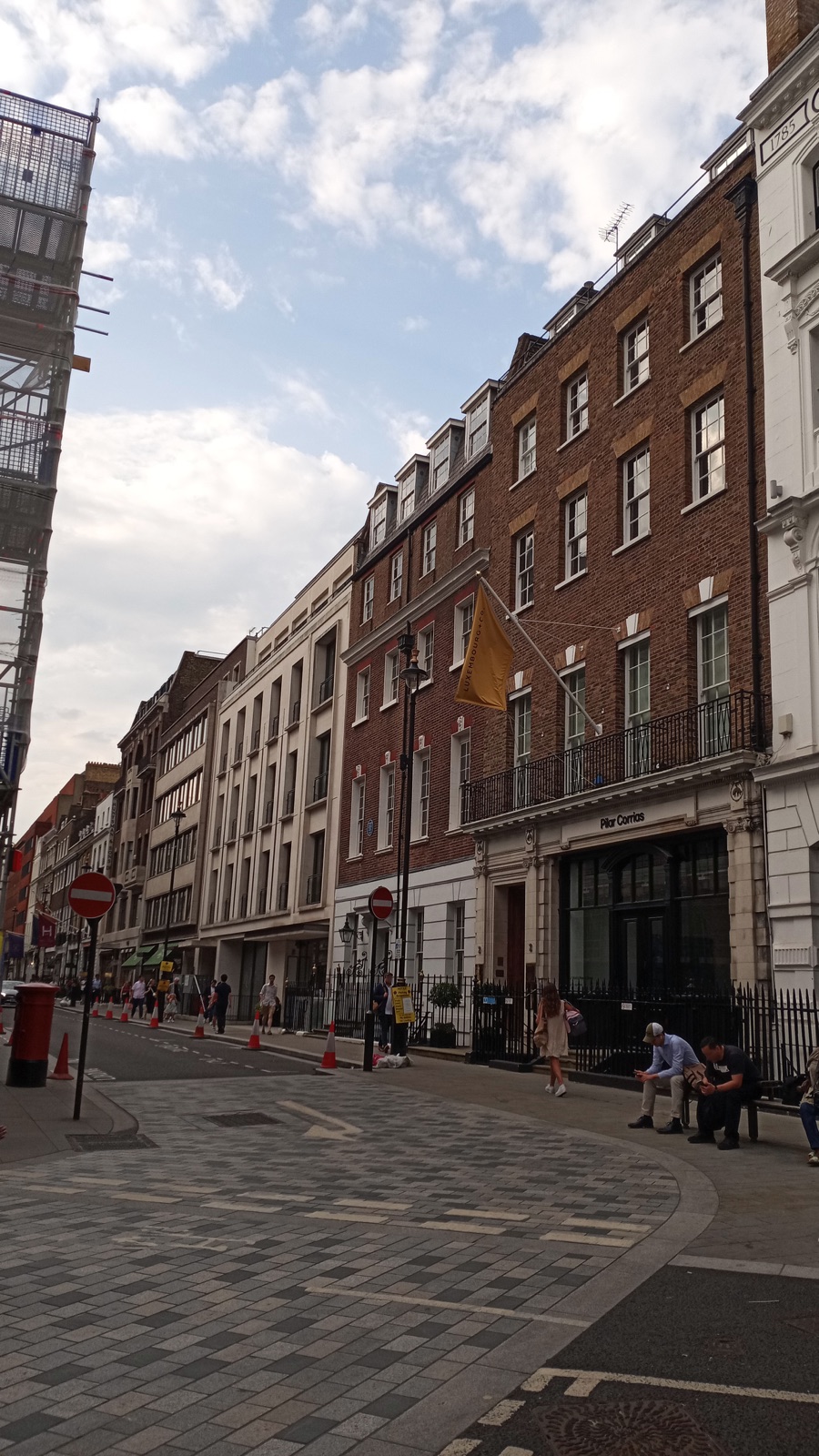 ถนน Savile Row ในกรุงลอนดอน มีอาคารอิฐแดงหลายชั้นหน้าต่างบานเลื่อน และท้องฟ้าครึ้มมีเมฆ