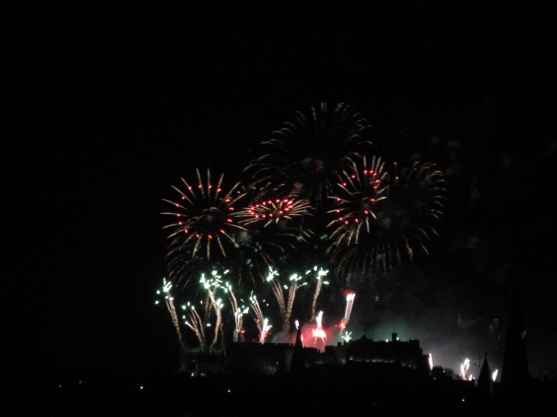 Pink, green and gold fireworks bursting over the dark silhouette of Edinburgh Castle on New Year's night
