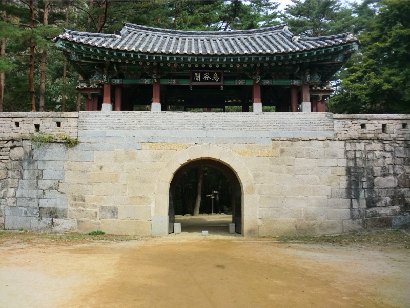 A stone gate with a Korean tiled roof standing in a pine forest on the old footpath over the Mungyeong Saejae pass, South Korea
