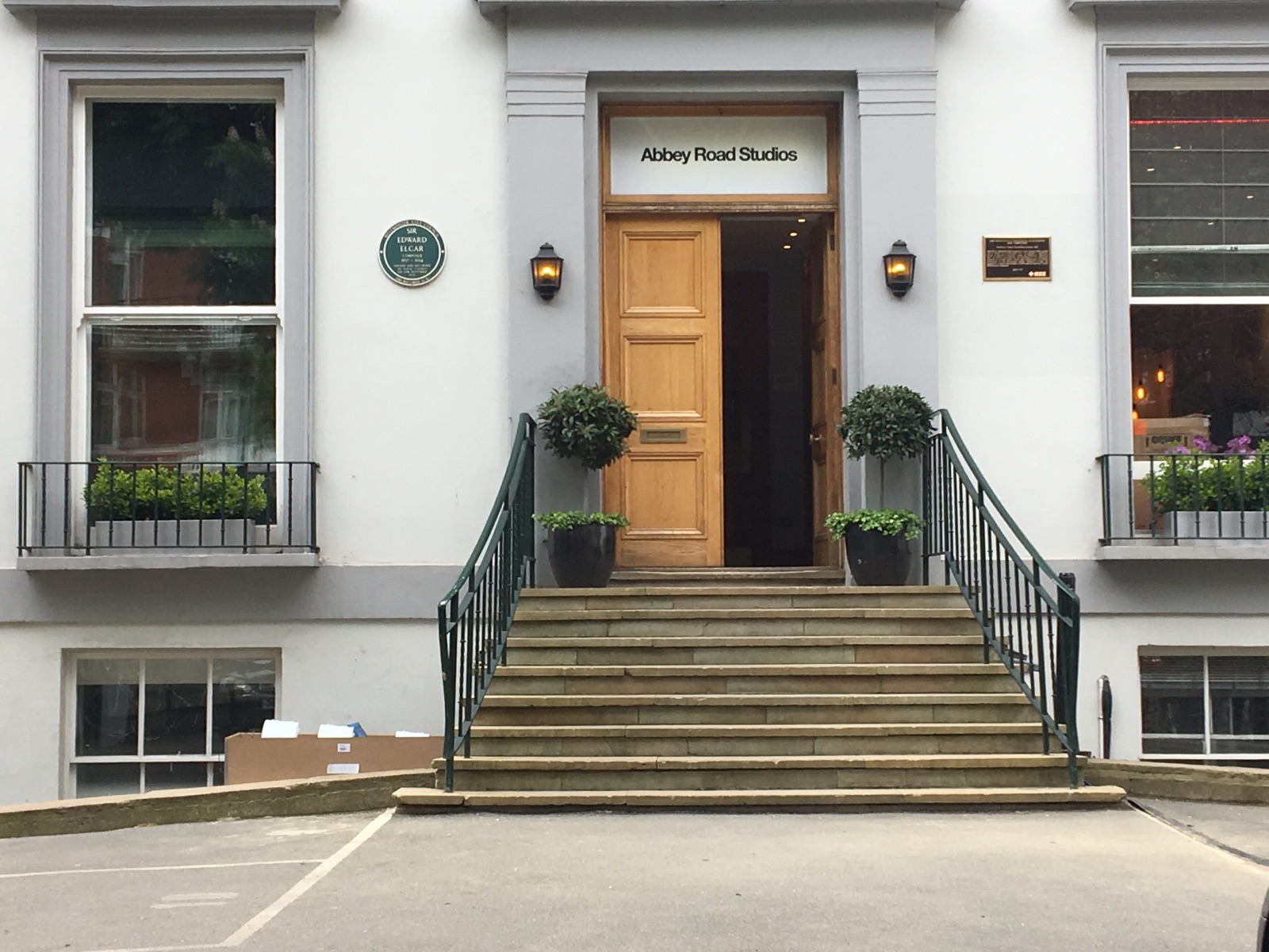 The entrance to Abbey Road Studios, with a name sign above the wooden door, stone steps and potted trees on both sides