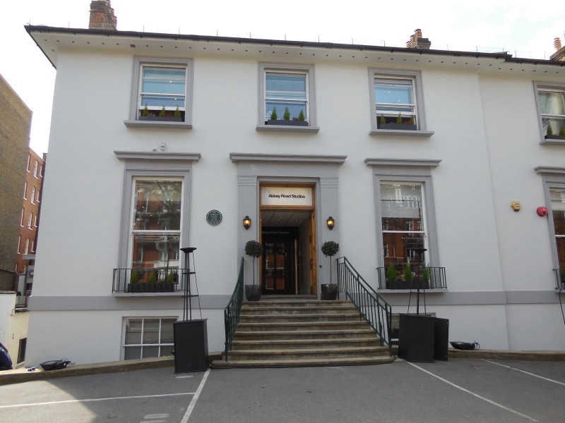 The white building of Abbey Road Studios in London, with steps up to the door and potted trees on both sides of the entrance