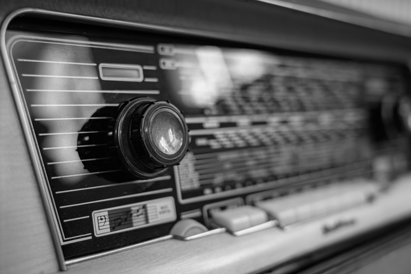 A close-up black-and-white photo of an old radio, showing a round knob and the frequency dial panel